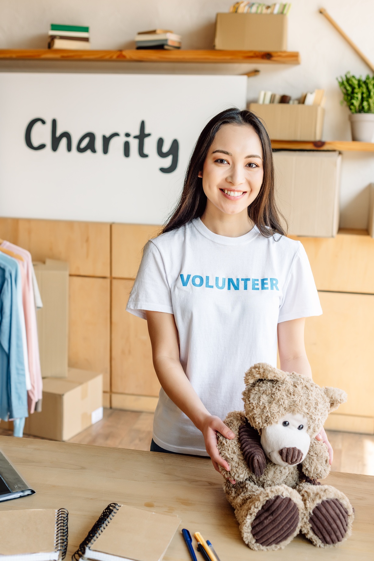 pretty asian volunteer girl holding teddy bear, smiling and looking at camera