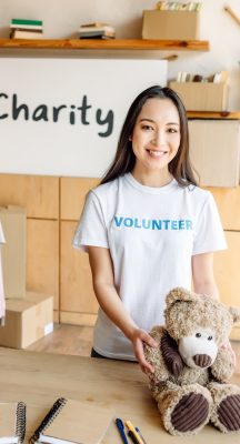 pretty asian volunteer girl holding teddy bear, smiling and looking at camera